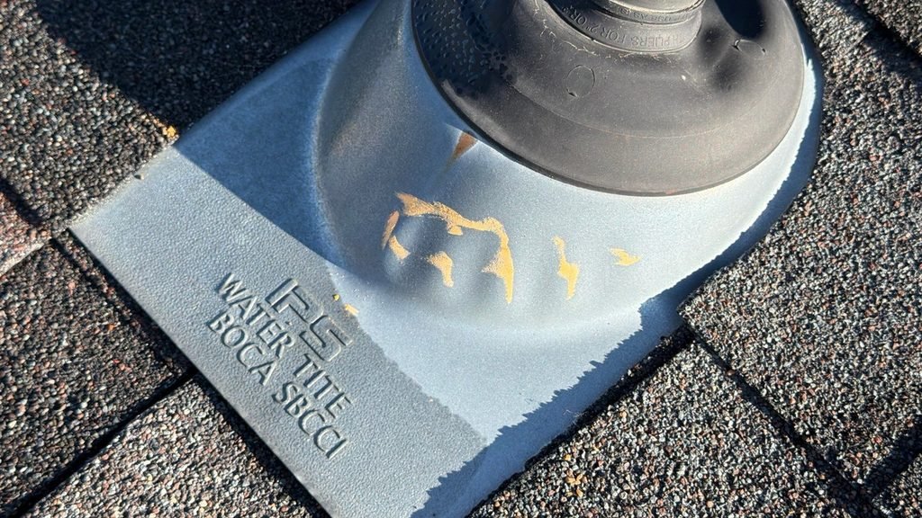 Dented metal plumbing vent boot with hail impact marks on a residential asphalt shingle roof.
