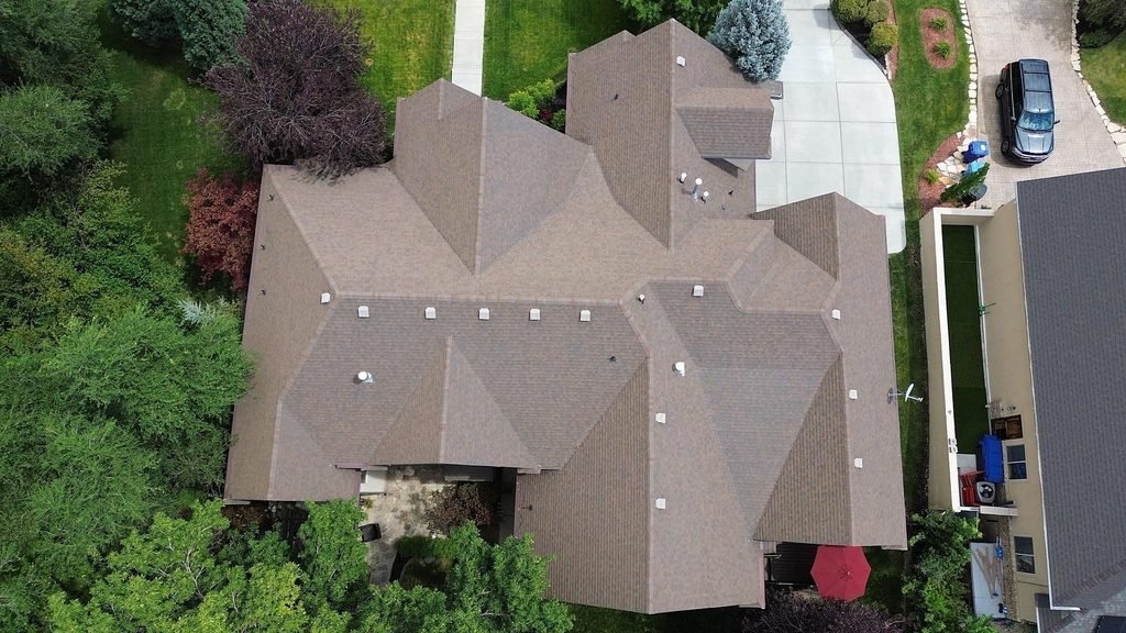 Overhead drone photo of a large Salt Lake County home with a brown hip roof made of many intersecting roof planes, valleys, and roof vents.