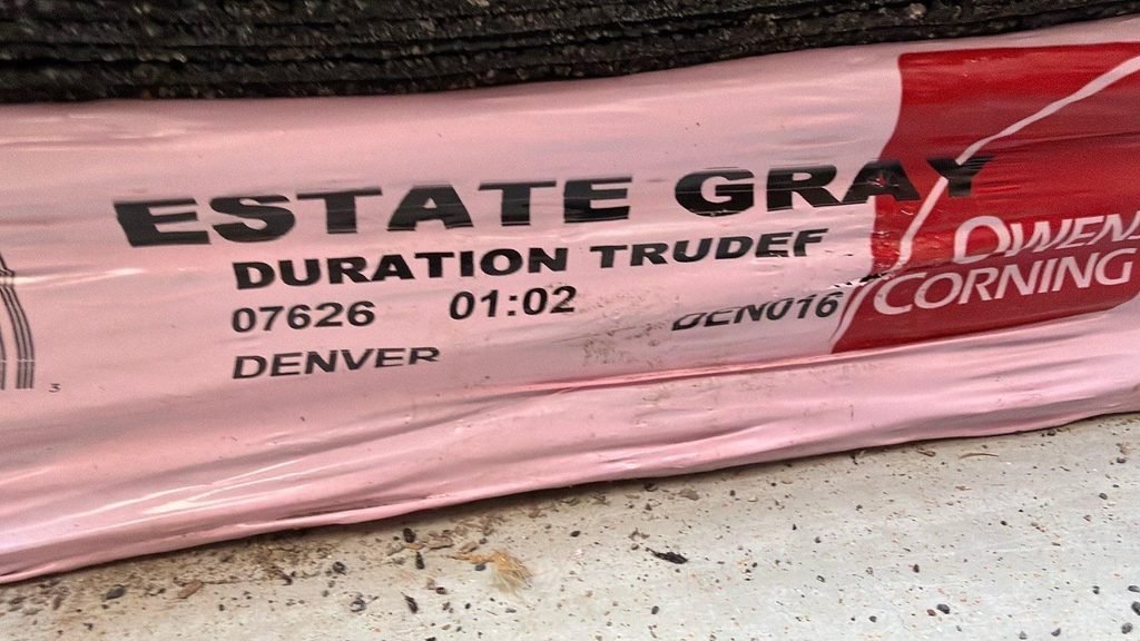 Close-up of a pink Owens Corning Duration TruDef architectural shingle bundle in the color Estate Gray on a Draper, Utah driveway.