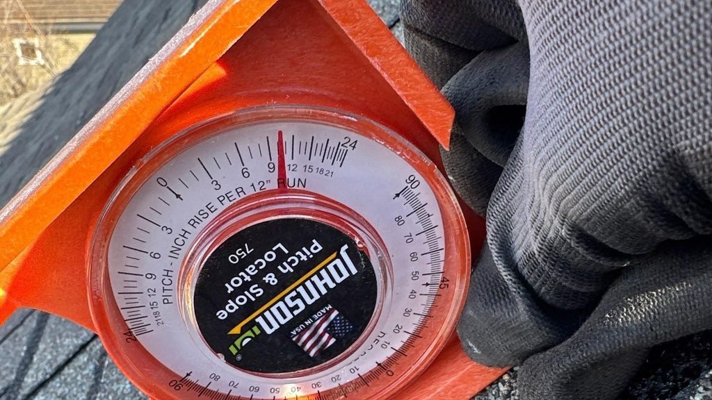 Orange pitch and slope locator held against asphalt shingles on a Mapleton, Utah roof, with a dial reading rise per 12 inches of run.