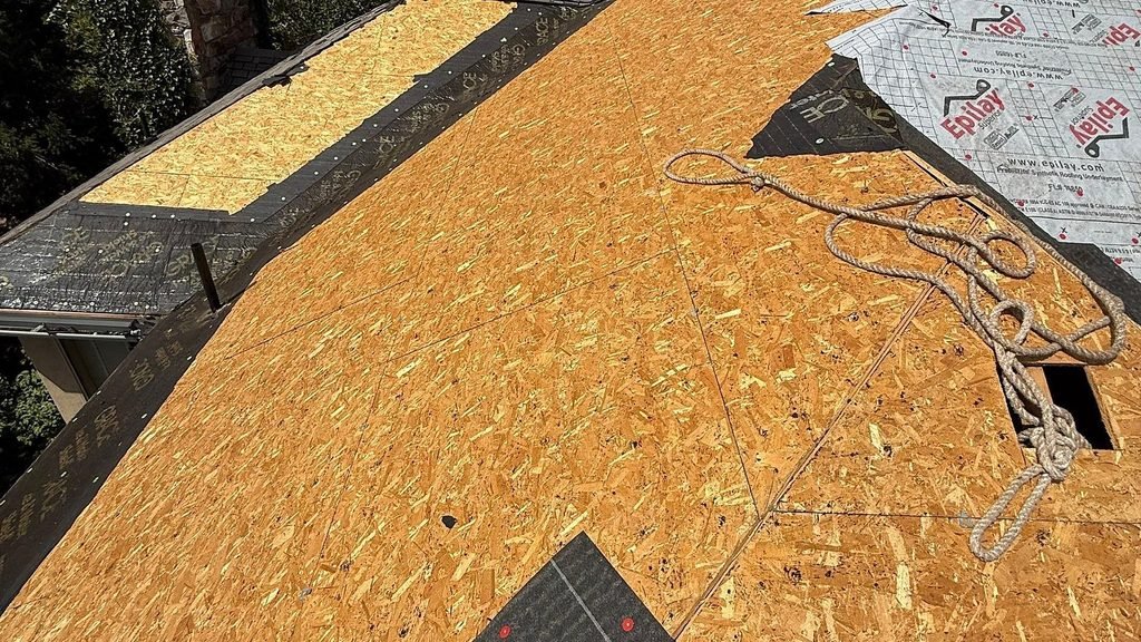 Bare OSB roof decking on an Alpine, Utah home during tear-off, with a strip of old shingles still at the lower edge and a safety rope coiled on the deck.