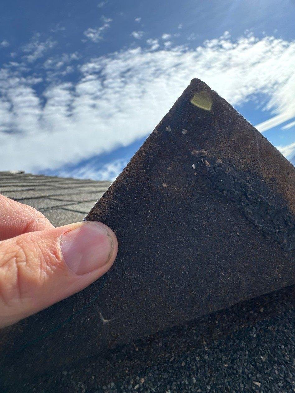 Hand holding up an architectural shingle tab to check its underside during a roof inspection in Lehi, Utah
