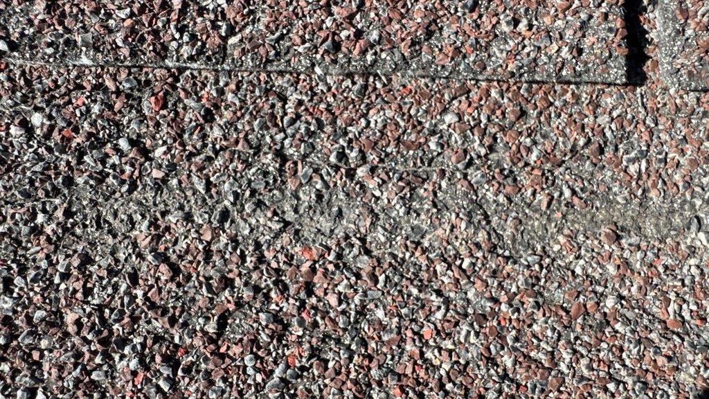 Close-up of asphalt shingles with worn, thinning granules on an aging roof